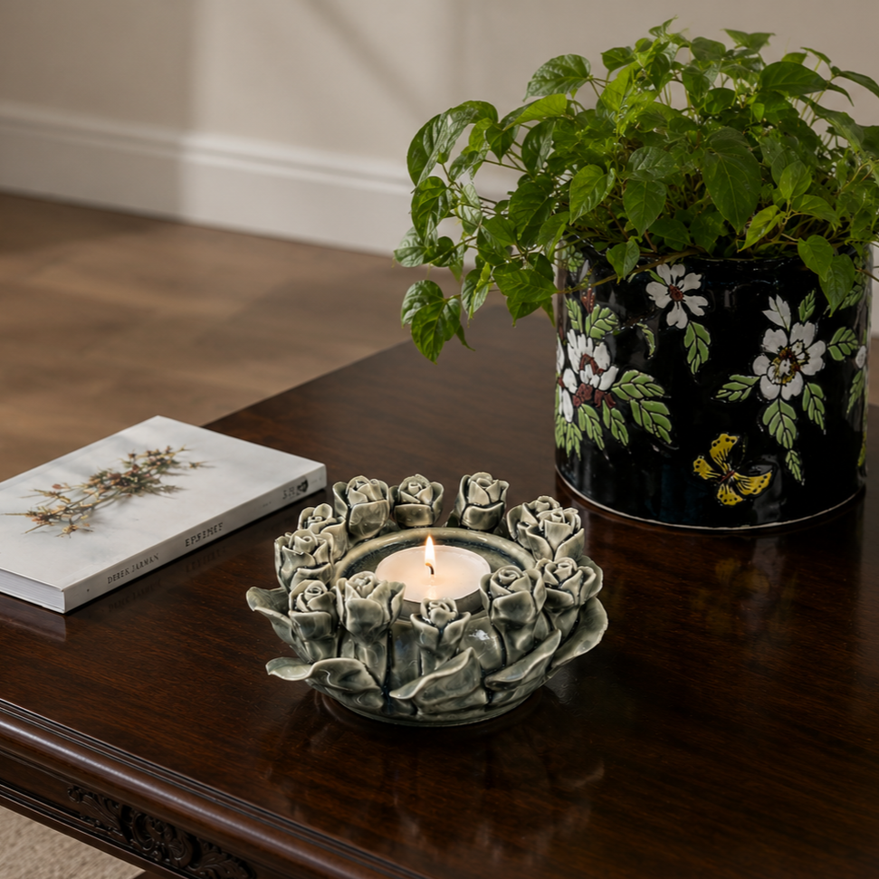 Handcrafted rose bud ceramic tealight holder placed on a polished dark wood table with a decorative floral planter in a cozy modern home setting.