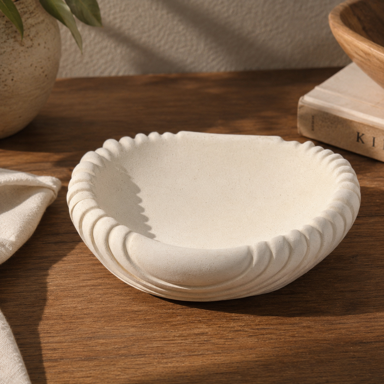 Minimalist scalloped white ceramic decorative bowl styled on a wooden table with soft natural lighting and neutral home décor accents.