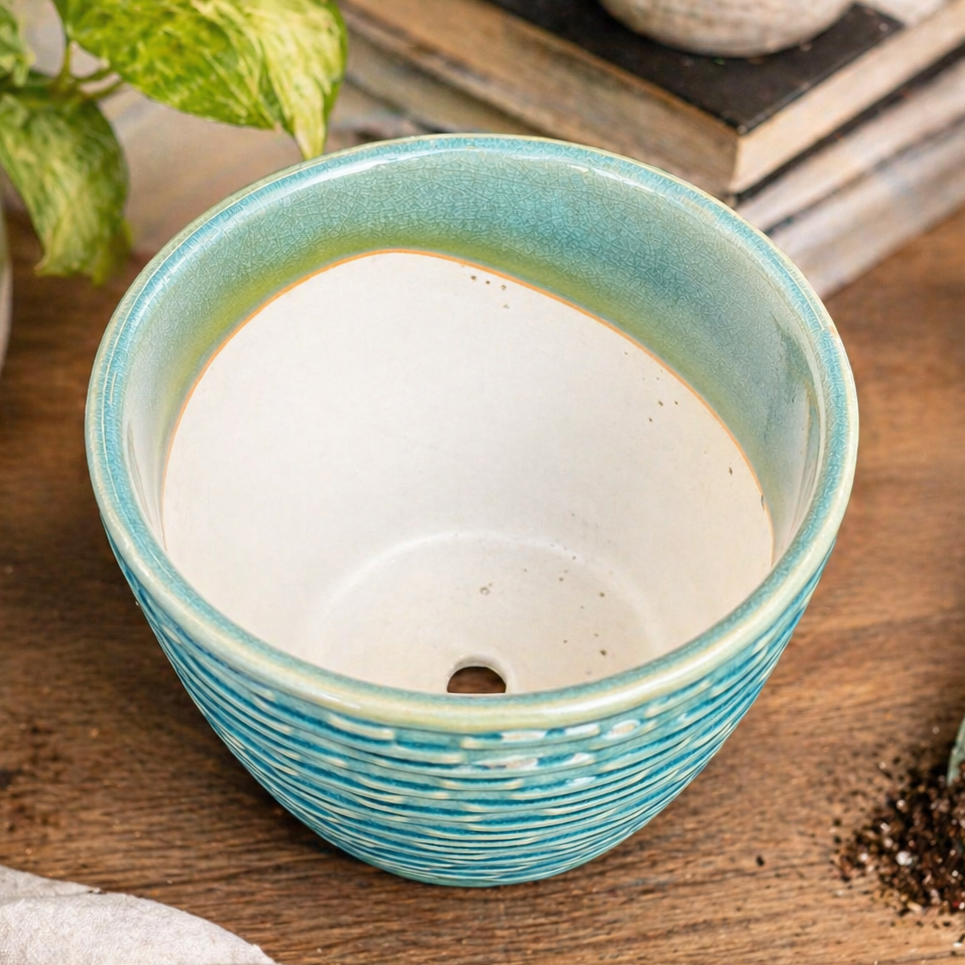 Close-up lifestyle image of a turquoise textured ceramic planter highlighting its inner glaze finish and drainage hole, styled on a wooden table with gardening elements.