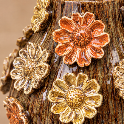 Close-up of brown glazed ceramic vase with raised orange, gold and cream 3D floral details