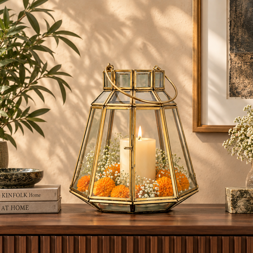 Luxury handcrafted brass and clear glass lantern styled with a lit pillar candle, orange marigolds, and baby's breath on a wooden console table in a premium contemporary home interior.