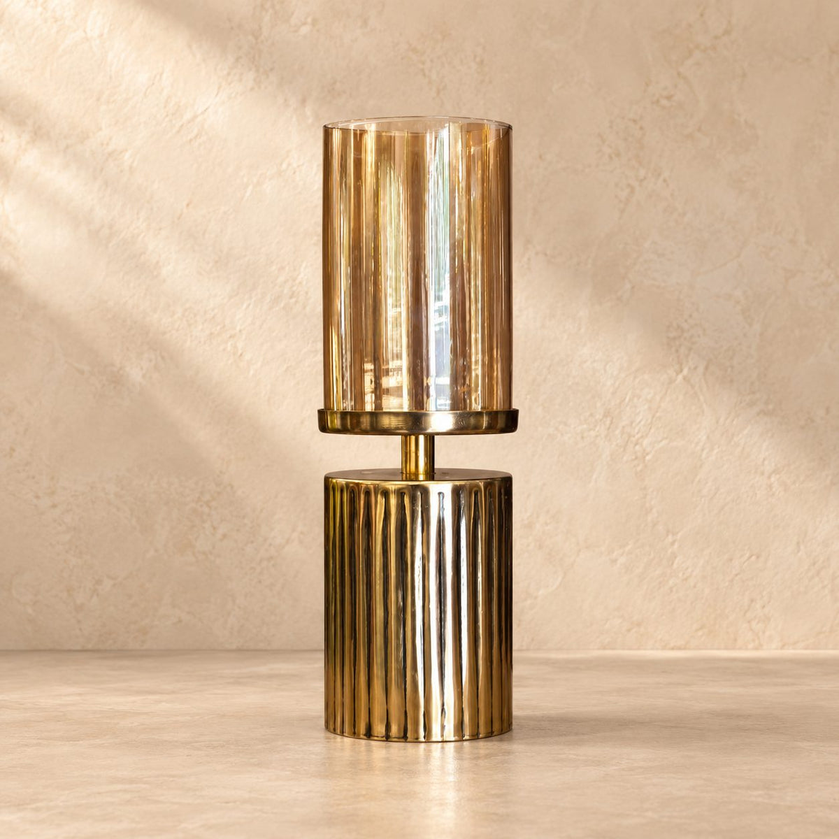 Amber glass hurricane candle holder with a ribbed gold metal base, handcrafted decorative candle stand for modern luxury interiors.