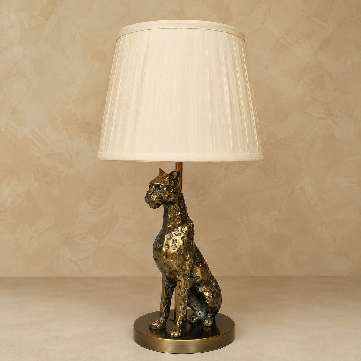 Antique brass leopard table lamp with a white pleated fabric lampshade on a neutral beige background by Inara Home Decor.