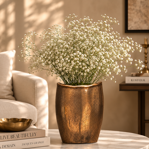 Antique bronze handcrafted metal vase styled with baby's breath flowers on a marble coffee table in a luxury living room.