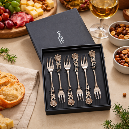 Antique Rose Dessert Forks Set of 6 in a premium gift box displayed on a warm beige Venetian seamless matte microcement surface with gourmet food and wine, luxury stainless steel servingware by Inara Home Decor.