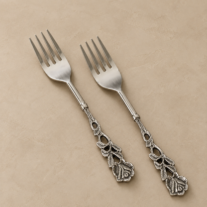 Antique Rose stainless steel dessert forks set of 2 with ornate floral handles displayed on a warm beige seamless matte microcement surface for luxury table setting by Inara Home Decor.