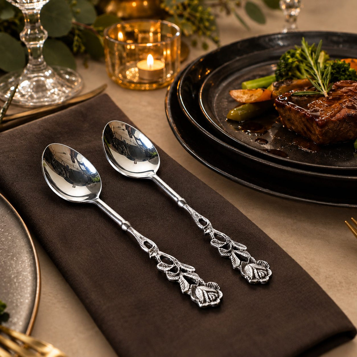 Antique Rose Silver Dessert Spoons Set of 2 displayed on a dark linen napkin with a luxury dining table setting on a warm beige Venetian seamless matte microcement surface.