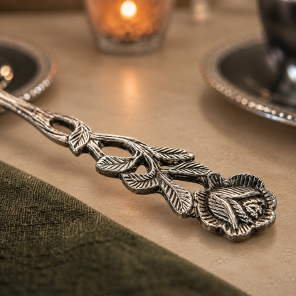 Antique Rose silver serving spoon with an intricate floral handle displayed on a warm beige Venetian seamless matte microcement surface, styled for a luxury dining table.