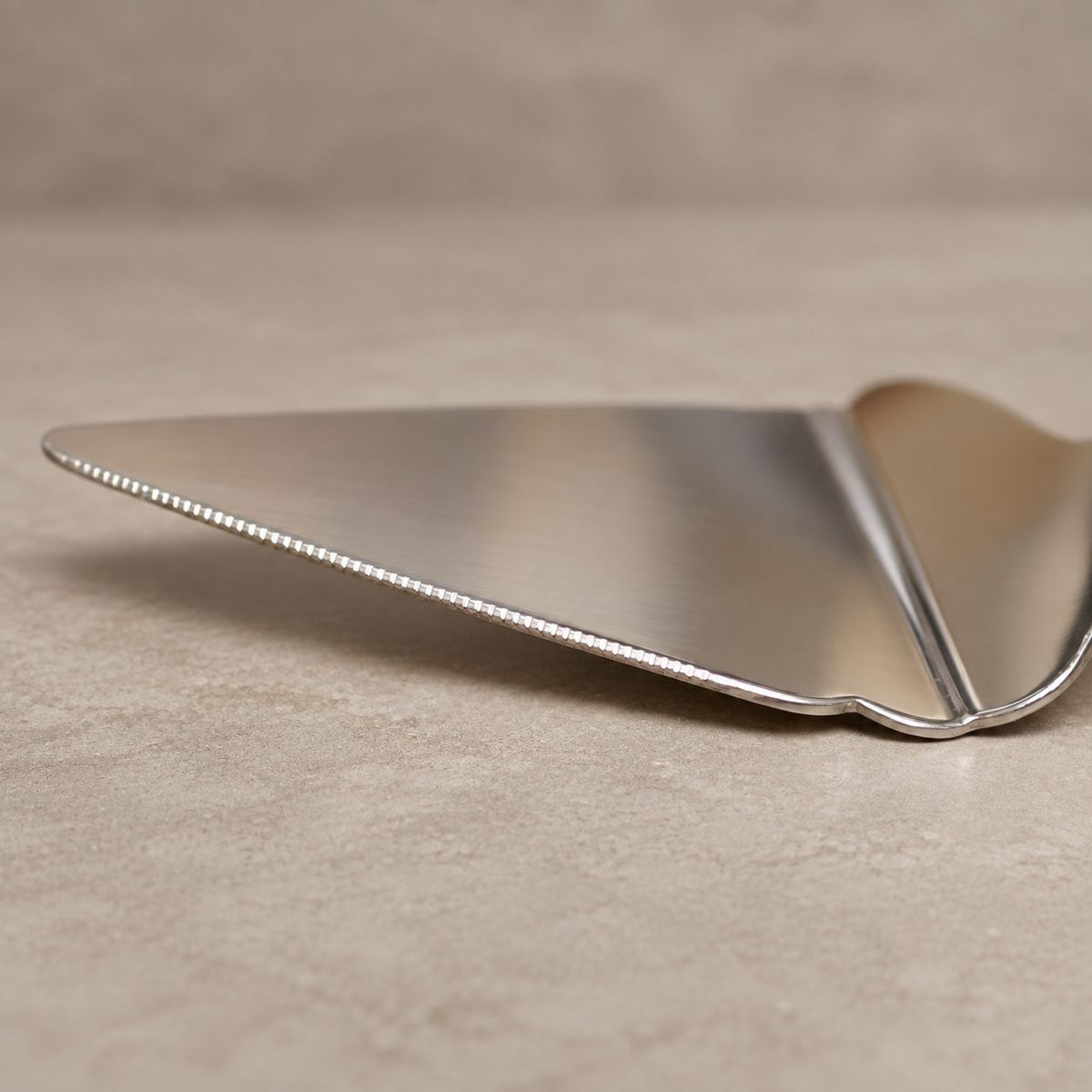 Close-up of the serrated edge on the Antique Rose stainless steel cake server with an elegant floral handle by Inara Home Decor.