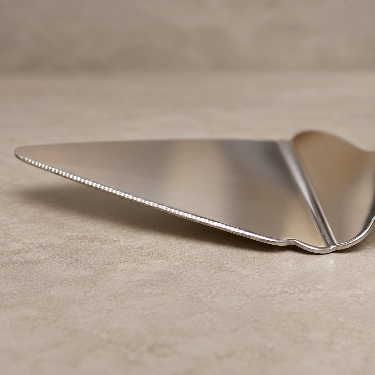 Close-up of the serrated edge on the Antique Rose stainless steel cake server with an elegant floral handle by Inara Home Decor.