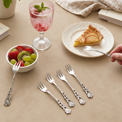 Antique Rose stainless steel dessert forks set of 6 with decorative floral handles, elegantly styled on a warm beige Venetian seamless matte microcement tabletop alongside fresh fruit, sparkling drink, and dessert for a premium dining setting.