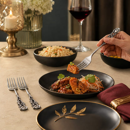 Antique Rose stainless steel table forks set of 2 with decorative floral handles styled on a warm beige Venetian seamless matte microcement dining table alongside elegant black dinnerware and gourmet meal.