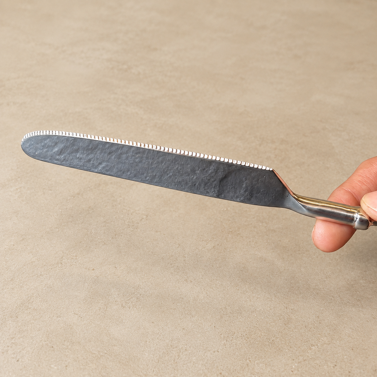 Antique Rose stainless steel table knife with an elegant floral brass handle displayed on a warm beige Venetian seamless matte microcement surface, luxury flatware by Inara Home Decor.