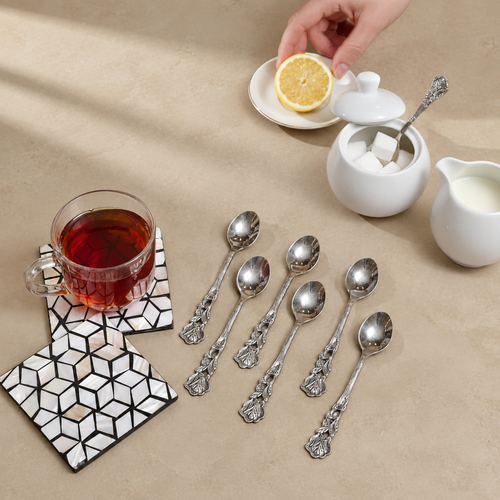 Set of 6 antique silver coffee spoons with ornate floral handles displayed on a warm beige Venetian seamless matte microcement surface alongside a tea cup, sugar bowl, milk jug, and lemon, ideal for elegant tea and coffee serving.