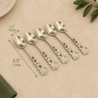 Antique silver dessert spoon set of 6 with ornate floral handles, measuring 5.5 inches long and 1.1 inches wide, displayed on a warm beige stone surface for luxury table setting by Inara Home Decor.