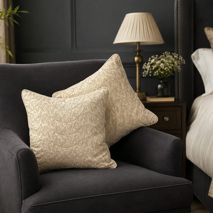 Beige embroidered cushion covers placed on a dark grey accent chair in a modern bedroom, featuring elegant textured embroidery for luxury home décor.