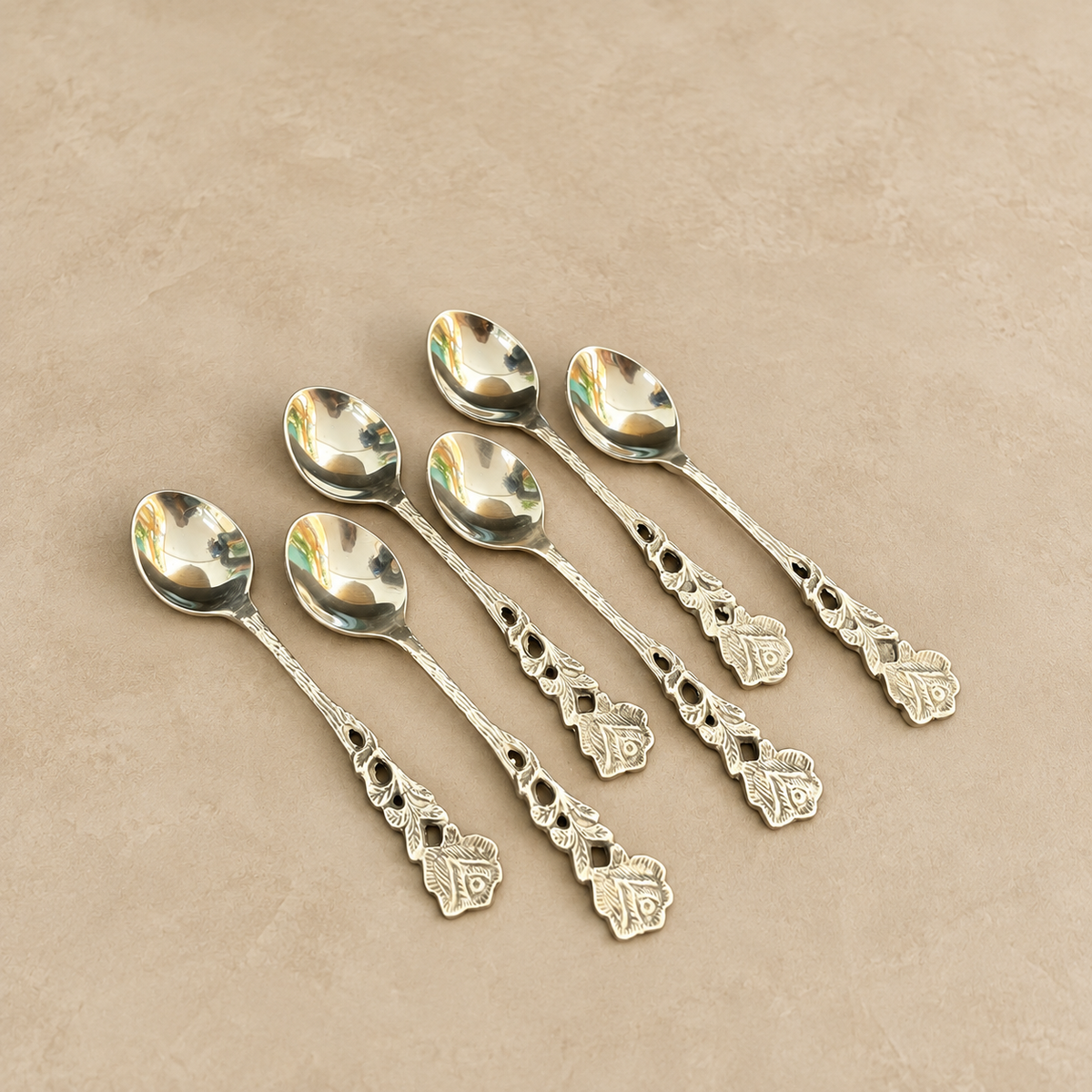 Antique silver floral tea spoons set of 6 with ornate vintage handles, premium stainless steel dessert and coffee spoons displayed on a warm beige Venetian matte microcement surface, luxury tableware by Inara Home Decor.