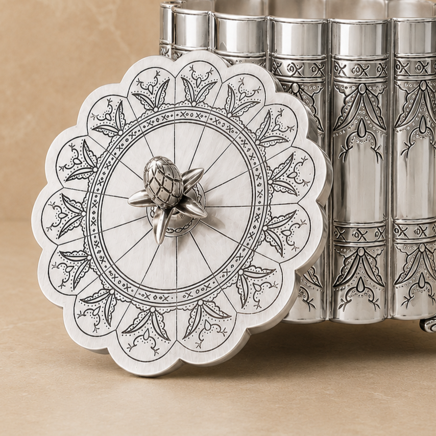 Antique silver ornate metal storage container with engraved scalloped lid displayed open on a beige studio background.