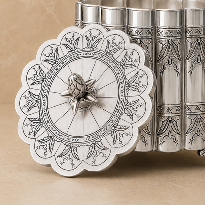 Antique silver ornate metal storage container with engraved scalloped lid displayed open on a beige studio background.