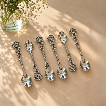 Antique silver rose handle teaspoon set of 6 arranged on a warm beige surface, featuring ornate floral handles and polished stainless steel bowls for elegant tea and coffee serving.
