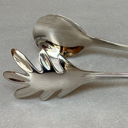 Close-up of antique silver salad serving spoon and fork set with polished finish and elegant curved design on neutral background