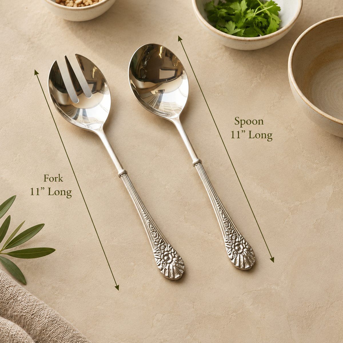 Antique silver serving spoon and fork set with ornate floral handles, each measuring 11 inches long, displayed on a warm beige Venetian seamless matte microcement surface with elegant olive green dimension arrows. Perfect for luxury table settings and servingware by Inara Home Decor.