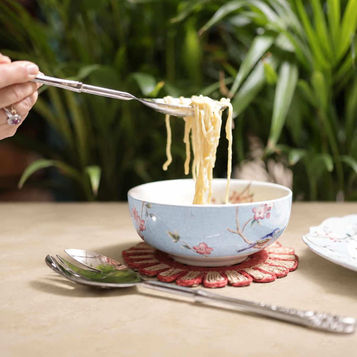 Antique Silver Serving Spoon and Fork Set with noodle bowl on a warm beige Venetian seamless matte microcement tabletop, luxury stainless steel servingware by Inara Home Decor.
