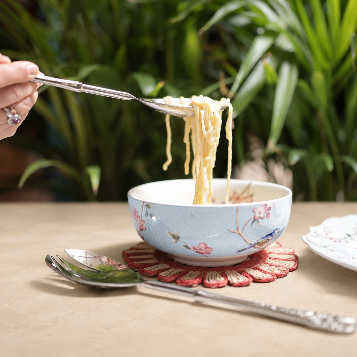 Antique Silver Serving Spoon and Fork Set with noodle bowl on a warm beige Venetian seamless matte microcement tabletop, luxury stainless steel servingware by Inara Home Decor.