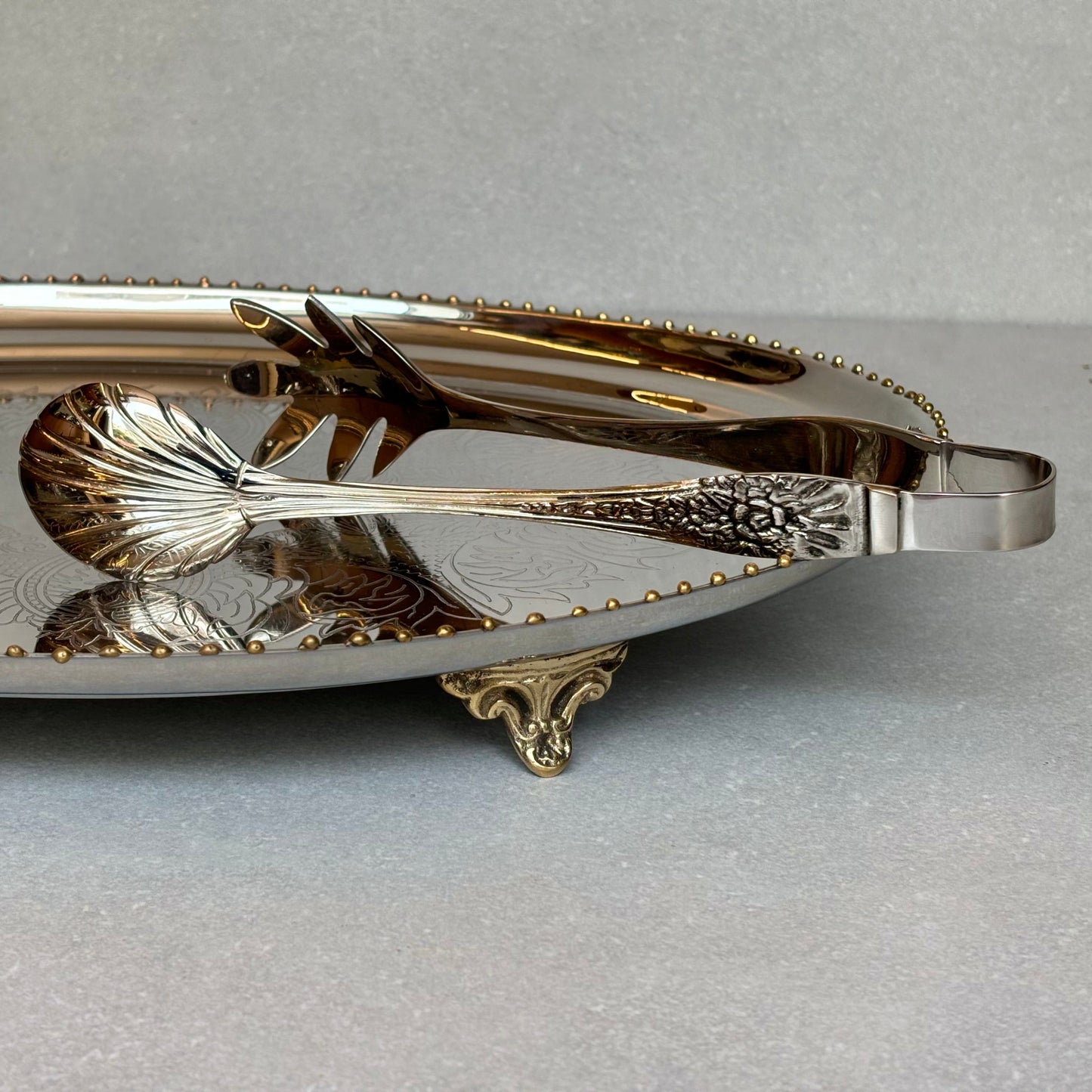 Antique silver serving tongs with intricate floral handle detailing placed on an ornate metal tray, ideal for serving desserts, salads, and buffet items.