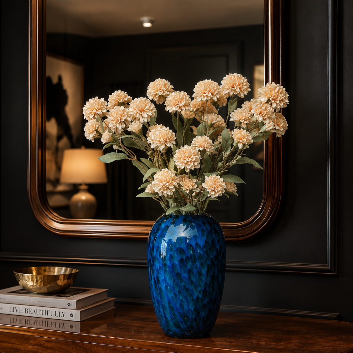 Artificial beige carnation flower stems displayed in a blue glass vase on a wooden console table with a decorative mirror in a luxury home interior.