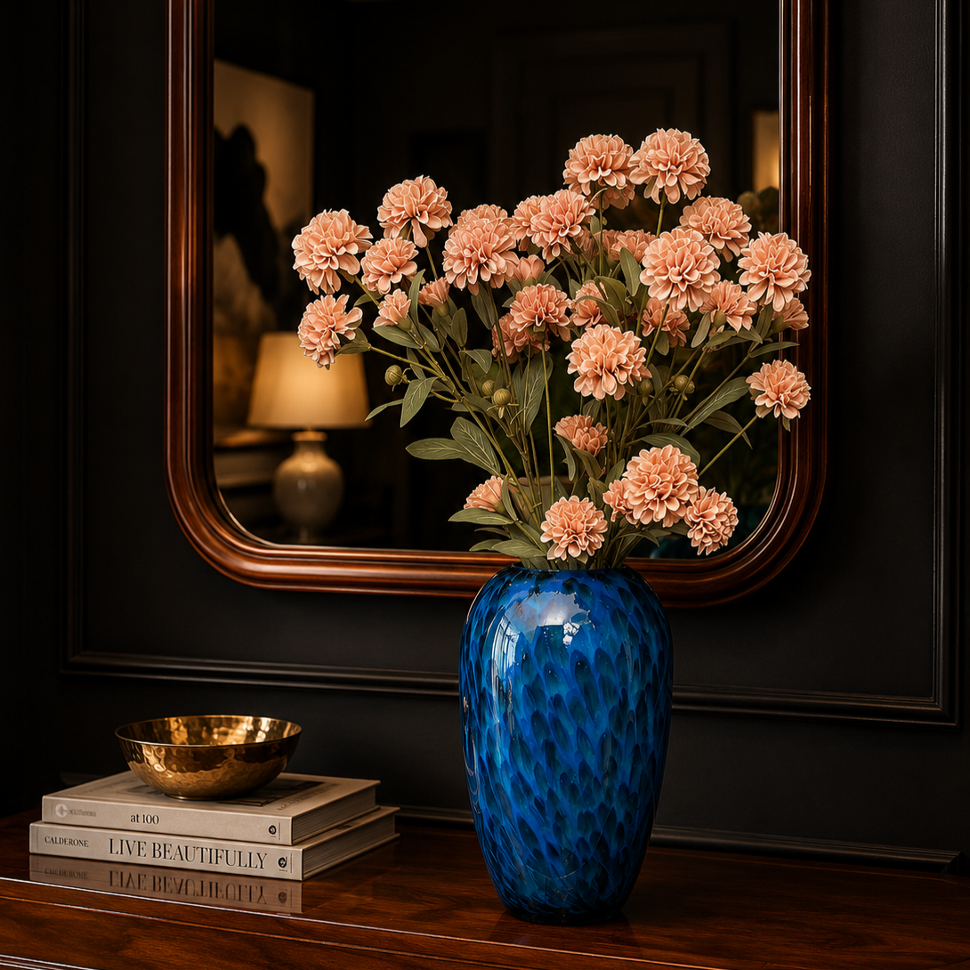 Artificial pink carnation flower stems arranged in a blue glass vase on a wooden console table with a decorative mirror in a luxury home interior.