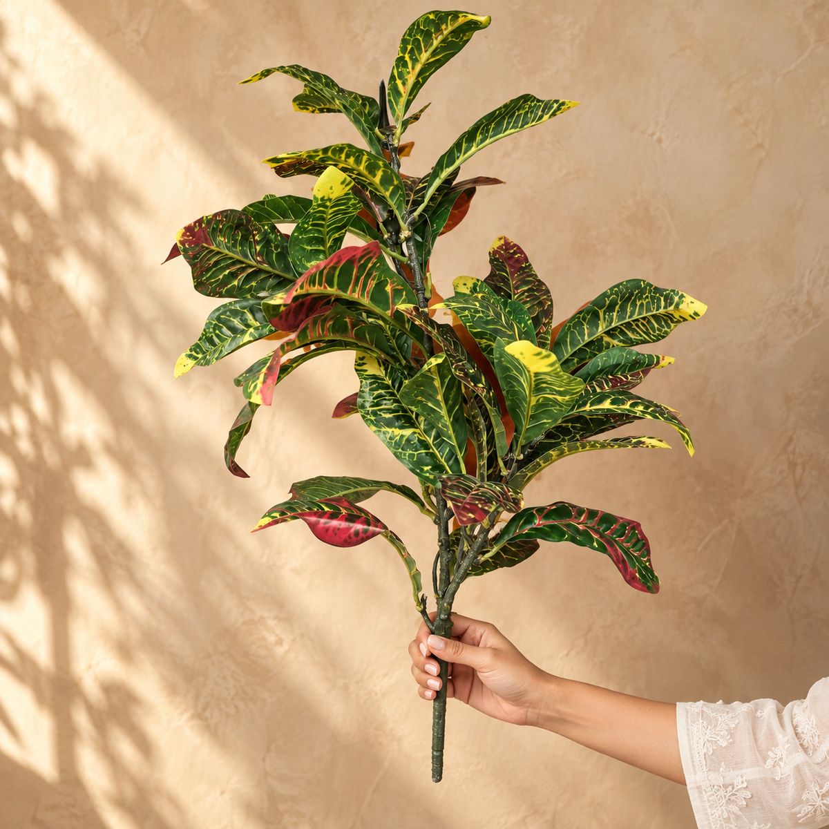Hand holding an Artificial Croton foliage bunch showing realistic size, lifelike multicoloured leaves and flexible stem.