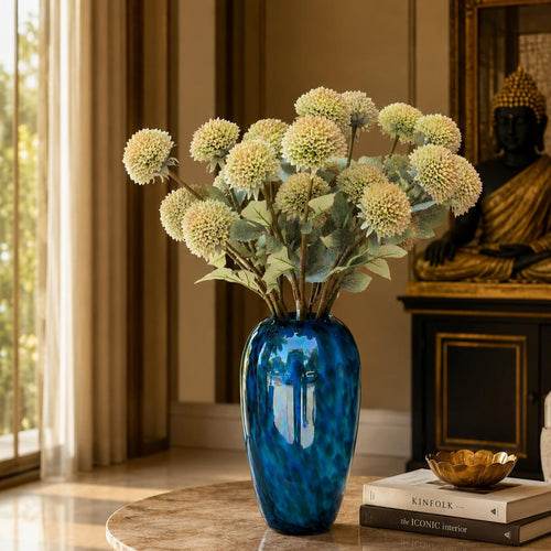 Artificial cream allium flower stems arranged in a blue glass vase on a luxury living room table with elegant home décor.