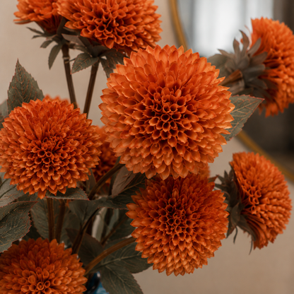 Close-up of realistic artificial orange dahlia blooms with detailed layered petals and natural-looking foliage.