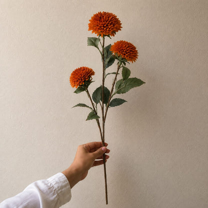 Single artificial orange dahlia stem with realistic layered petals and lifelike green foliage, perfect for elegant floral arrangements and home décor.