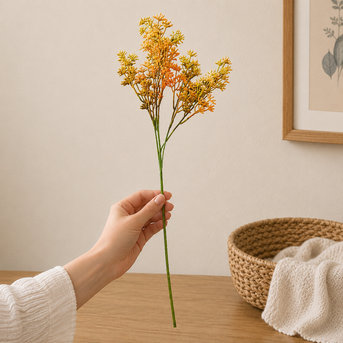 Close-up lifestyle image of a hand holding a single yellow and orange artificial floral stem against a neutral wall, showcasing the size, texture, and realistic botanical detailing.