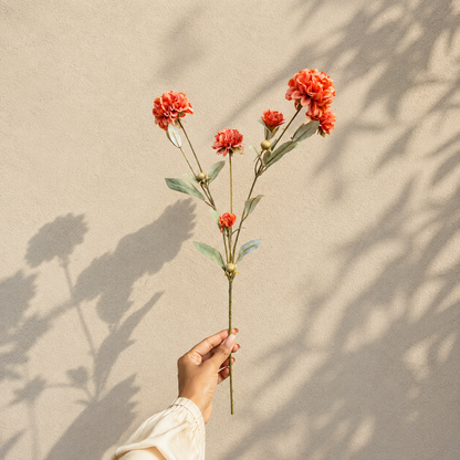 Hand holding a single artificial coral flower stem against a textured grey wall in natural daylight, showcasing the size and detailing of the bloom.