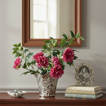 Artificial pink peony flower stems arranged in a decorative silver vase on a wooden console table for elegant home décor.