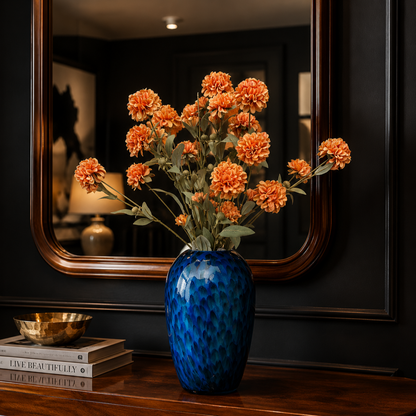 Artificial orange carnation flower stems arranged in a blue glass vase, creating a vibrant luxury floral display for living room, console table, and home décor styling.