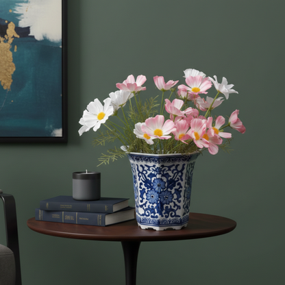 Artificial pink and white cosmos flowers arranged in a blue and white ceramic planter on a side table with modern home décor.