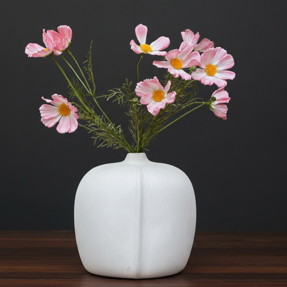 Artificial pink cosmos flower stems displayed in a white textured ceramic vase against a black background.