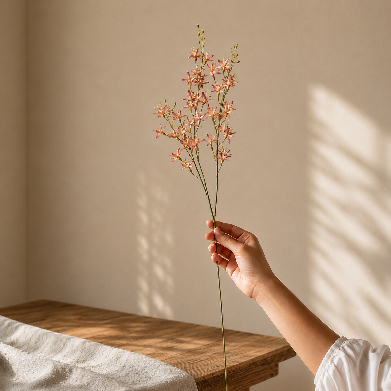 Artificial pink wildflower stem held in hand, premium faux floral branch for elegant home décor and vase arrangements.