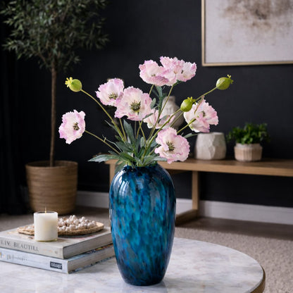 Artificial Poppy Pink stems arranged in a blue glass vase on a coffee table for elegant home décor.