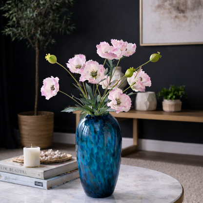 Artificial Poppy Pink stems arranged in a blue glass vase on a coffee table for elegant home décor.