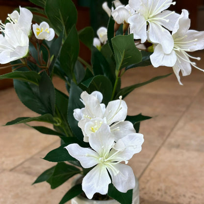 Close-up of realistic artificial white cherry blossom flowers with detailed petals and lush green foliage.