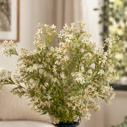 Artificial white wildflower bunch arranged in a blue ceramic vase on a wooden coffee table in a modern living room with soft natural light and elegant home décor.