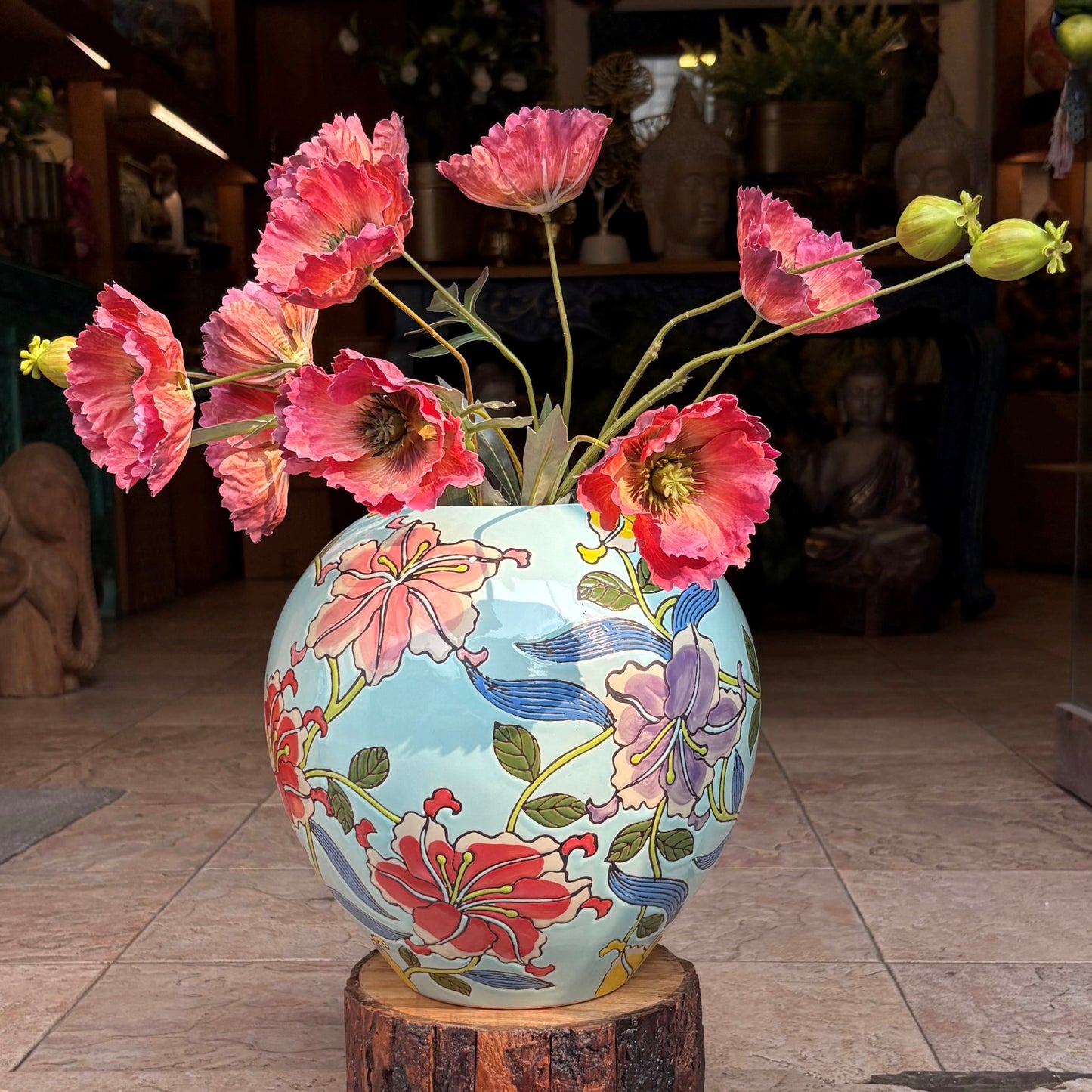 Close-up of a handcrafted ceramic jar with intricate floral artwork and red poppy flowers in an elegant indoor setting.