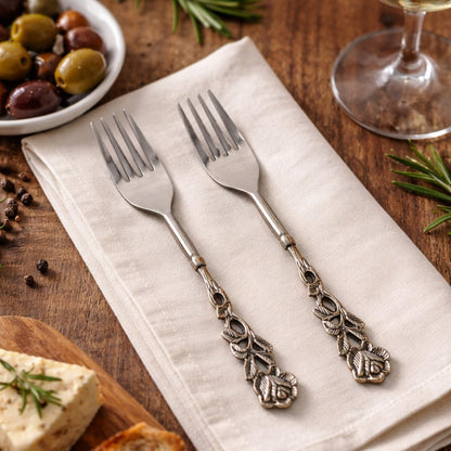 Elegant hand-painted silver forks resting on a cream-colored cloth napkin, styled with a side of olives and rosemary for a high-end editorial look.