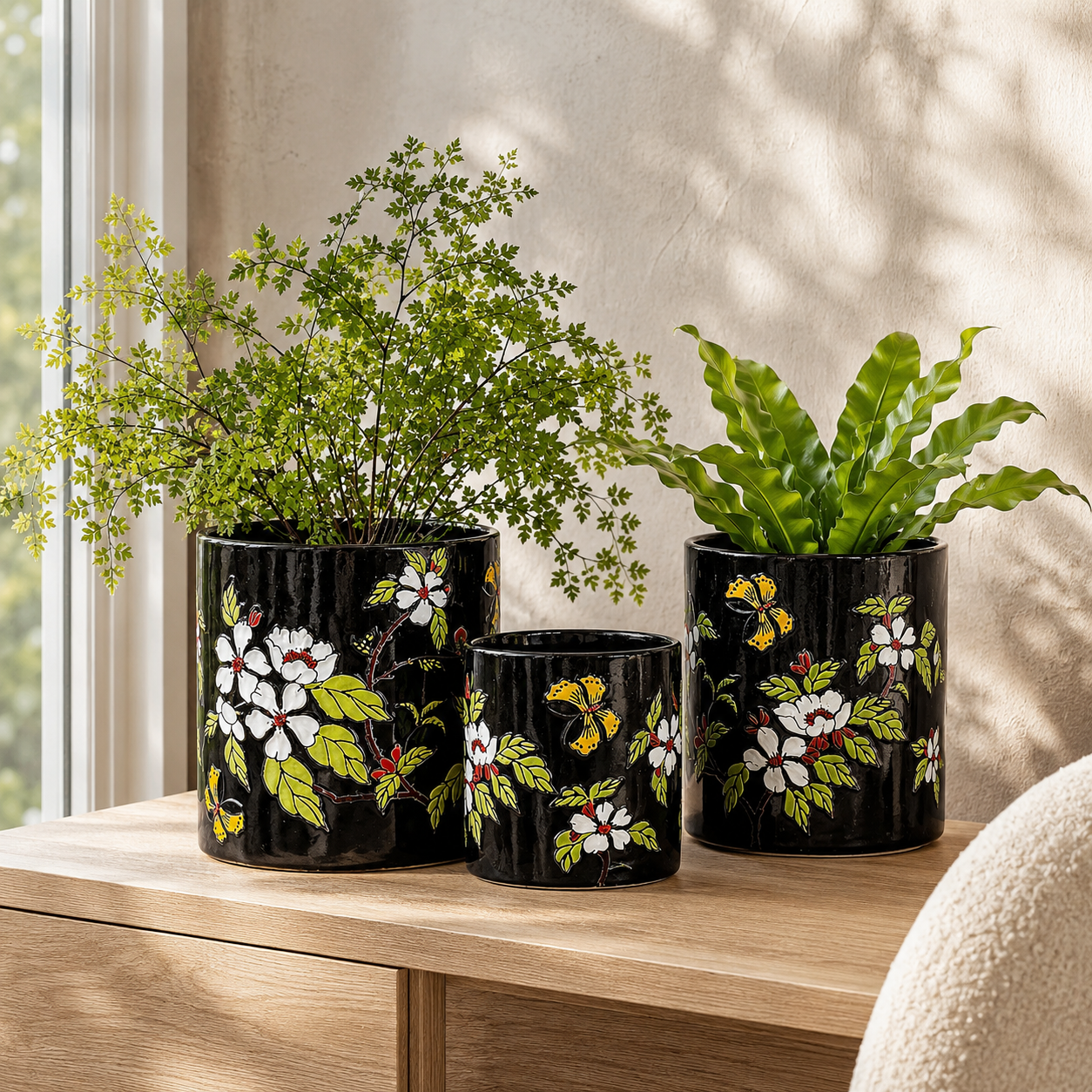 Black hand-painted floral ceramic planter set of 3 displayed on a wooden console with live indoor plants in a luxury modern home interior.