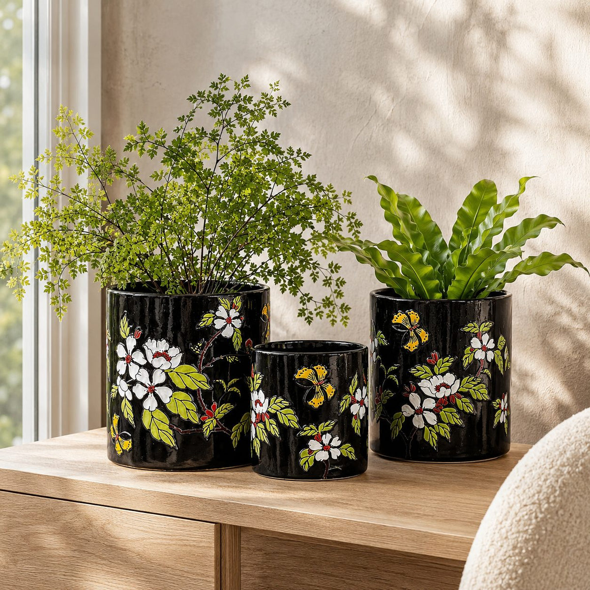 Black hand-painted floral ceramic planter set of 3 displayed on a wooden console with live indoor plants in a luxury modern home interior.